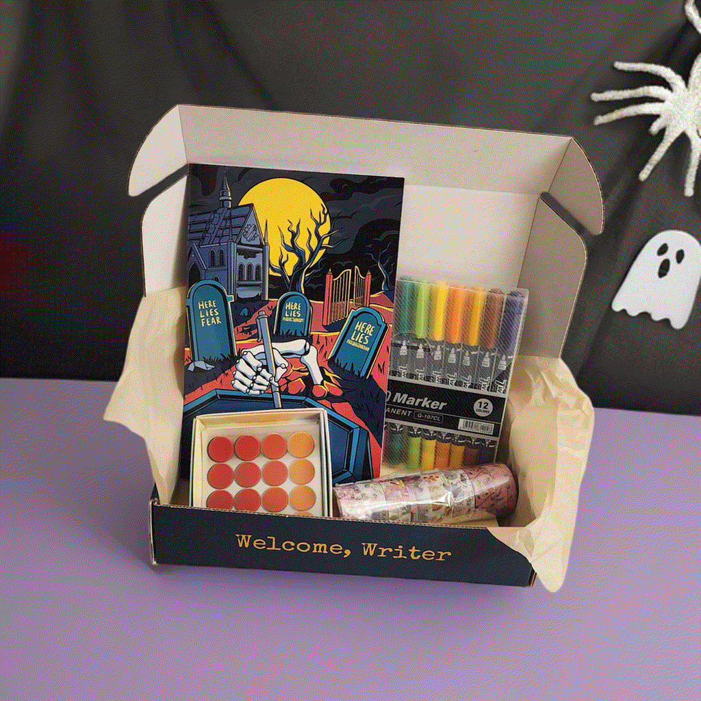 The subscription box for writers on a table of halloween decorations. Journal, stickers, and pens are visible inside.